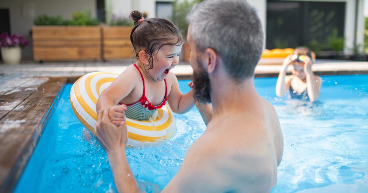 Father with happy daughter outdoors in the backyard, playing in swimming pool.